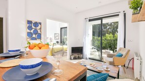 Uma sala de estar moderna com área de jantar, sofá, mesa de centro e uma janela grande com vista para o verde.