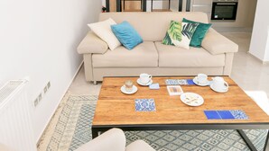Uma sala de estar moderna com um sofá, uma mesa de centro e uma cozinha ao fundo.