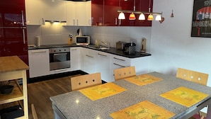 A modern kitchen with white and red cabinetry, a granite countertop, and a dining area with a table and chairs. - Great Views, Great Location, modern & cozy Apartment (renovated 2022) (Grindelwald)