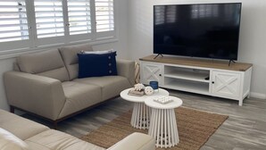 Ett vardagsrum med en beige soffa, ett vitt soffbord och en tv som står på ett träställ.