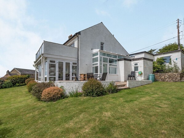A modern two-story house with a large glass front and a stone retaining wall. - Garna (Pwllheli)