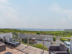 A balcony with outdoor furniture, a view of the sea, and distant hills. - Garna (Pwllheli)