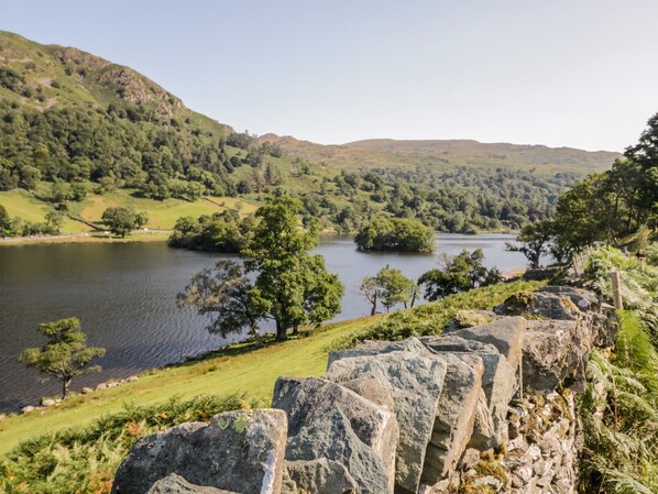 A stone wall with a view of a lake surrounded by hills and trees.