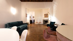 A spacious living room with a wooden floor, a green sofa, a white table, and pink chairs. - Chic and Style in Historical Via Giulia (Roma)