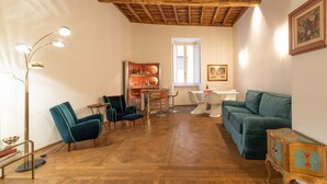 A spacious living room with a wooden ceiling, a green sofa, a dining area with a white table, and a bookshelf. - Chic and Style in Historical Via Giulia (Roma)