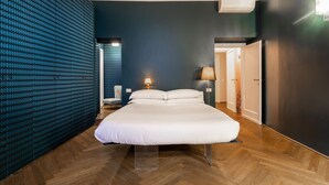 A modern hotel room with a large bed, a wooden herringbone floor, a dark blue accent wall, and a patterned wall on one side. - Chic and Style in Historical Via Giulia (Roma)