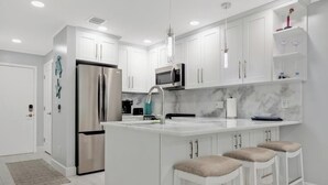 Una cocina moderna con armarios blancos, electrodomésticos de acero inoxidable, una encimera de mármol y taburetes de bar.