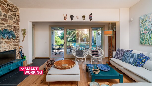 A modern living room with a stone wall, a sofa, a TV, and a dining area with chairs and a table. - Casa Loris by Wonderful Italy (Olbia)