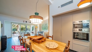 A modern kitchen with built-in ovens, a dining area with wooden furniture, and a view of the outdoors. - Casa Loris by Wonderful Italy (Olbia)