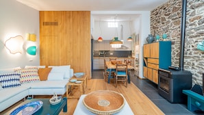 A modern living room with a sofa, coffee table, and a dining area with chairs and a table. A kitchen with a stove and cabinets is visible in the background. - Casa Loris by Wonderful Italy (Olbia)