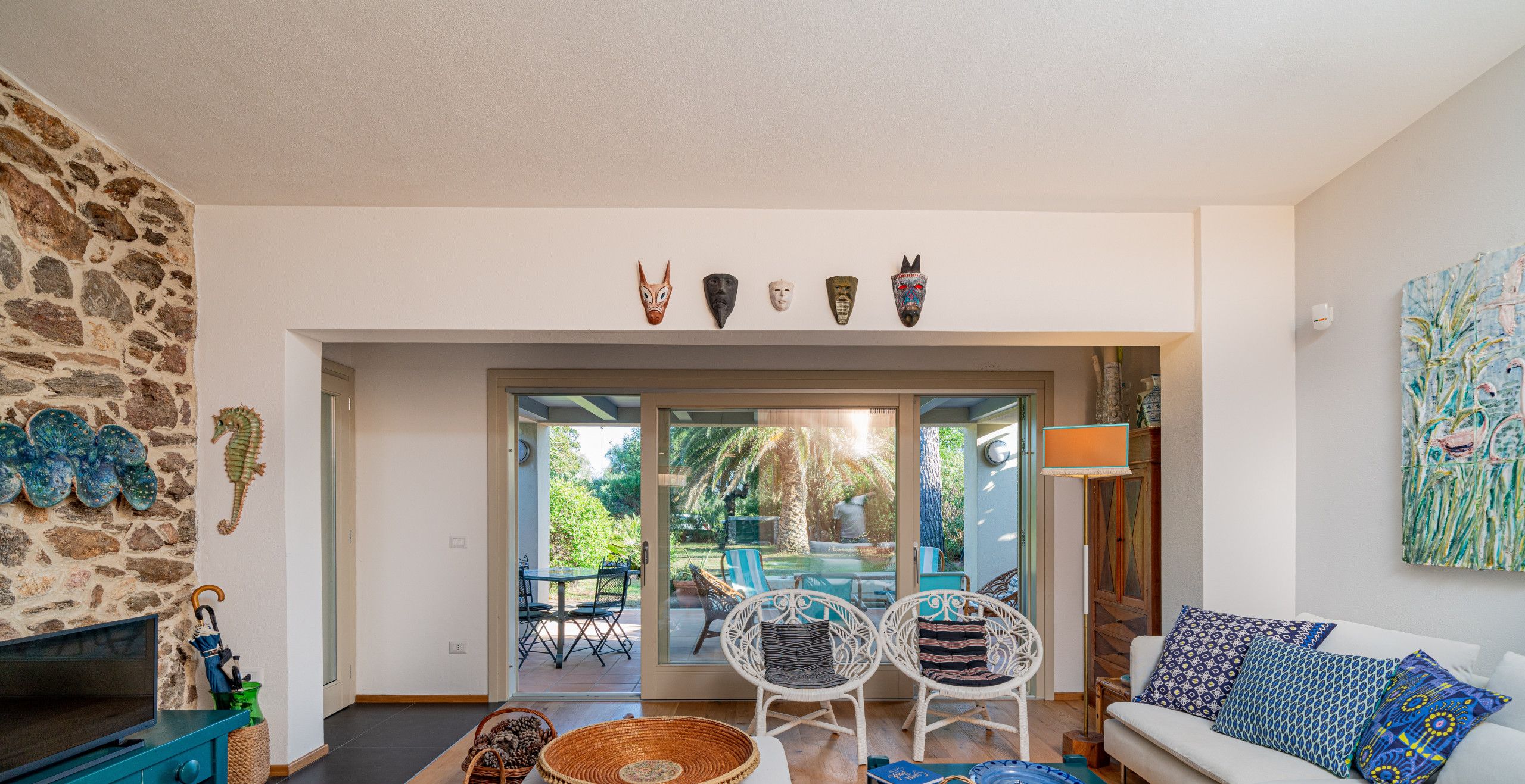 A modern living room with a stone wall, a sofa, a TV, and a dining area with chairs and a table.