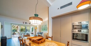 Une cuisine moderne dotée de fours encastrés, un coin repas avec des meubles en bois et une vue sur l’extérieur.