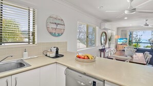 Una cocina moderna con lavavajillas Bosch, un comedor con mesa y sillas, y vista al mar a través de amplios ventanales.