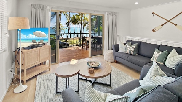 Una sala de estar moderna con televisor, sofá, mesa de centro y vistas a un balcón con mobiliario exterior.