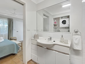 Ein modernes Badezimmer mit einem weißen Waschbecken, einem Spiegel und einer integrierten Waschmaschine.