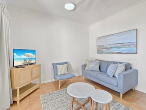 Un salon comprenant un canapé, deux fauteuils, une table basse, un téléviseur posé sur un meuble en bois et un tableau accroché au mur.