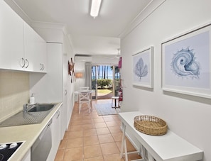 A kitchen with white cabinets, a sink, and a dining area with a table and chairs. There are framed artworks on the walls and a view of the outdoors.