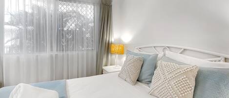 Habitació d'hotel amb llit, una tauleta de nit, una làmpada i una finestra amb cortines.