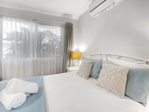 Ein Hotelzimmer mit einem Bett, einem Nachttisch, einer Lampe und einem Fenster mit Vorhängen.