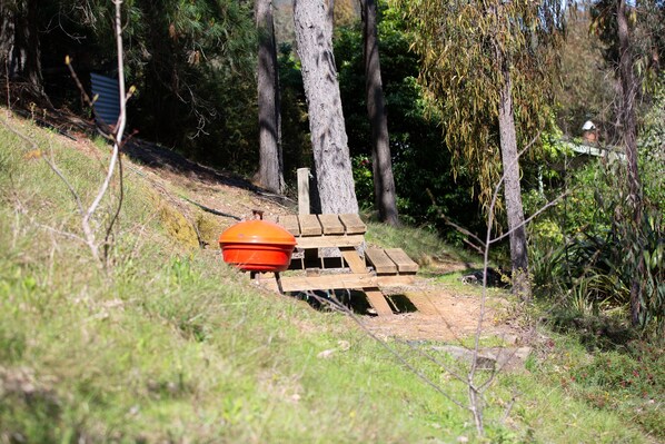 Un banco de madera con un objeto naranja encima, rodeado de  árboles y hierba.