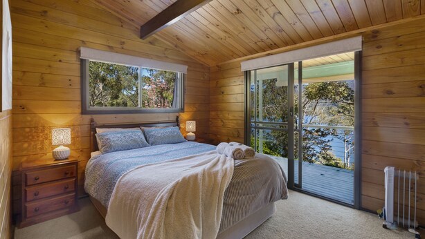 Une chambre avec un grand lit, des murs en bois, une fenêtre et une porte-fenêtre coulissante donnant sur un balcon.