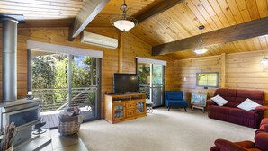 L'intérieur d'un chalet en bois comprend une cheminée, un téléviseur et un coin salon.