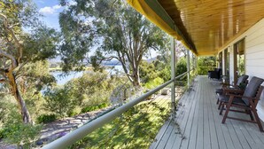 Une terrasse en bois avec des sièges extérieurs, offrant une vue sur un lac et des arbres.
