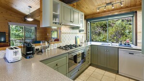 Une cuisine avec des meubles en bois, une cuisinière, un lave-vaisselle et une fenêtre donnant sur un paysage verdoyant.