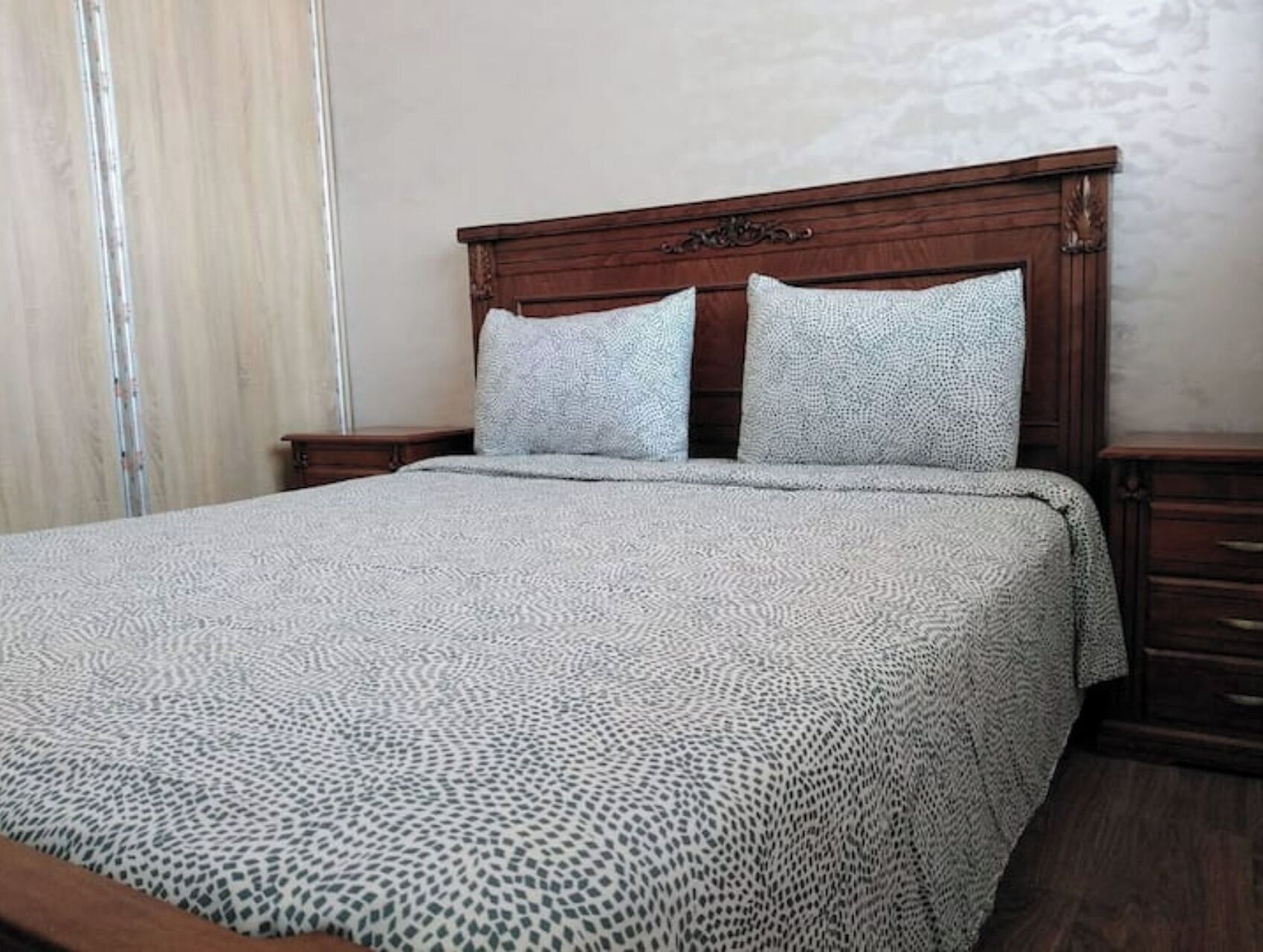 A bed with a patterned bedspread, a wooden headboard, and two bedside tables.