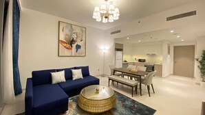 Un salon moderne avec un canapé bleu, une table basse en verre et un coin repas agrémenté d’une banquette.