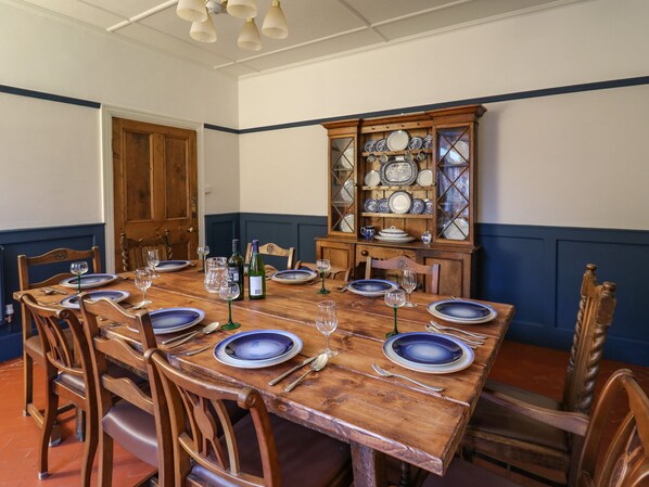 Une salle à manger avec une table en bois dressée pour six personnes, entourée de chaises en bois. On aperçoit, au fond, une vitrine contenant de la vaisselle bleue et blanche.