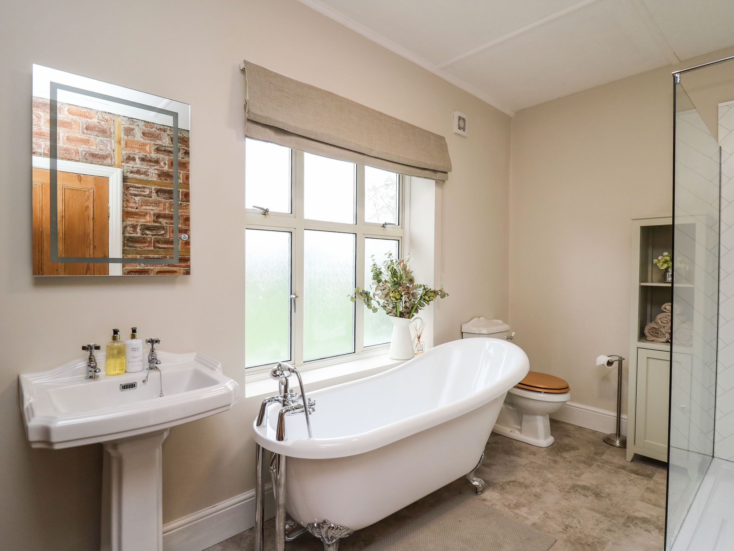 A bathroom with a freestanding bathtub, a sink, a toilet, and a window with a view of the outdoors.