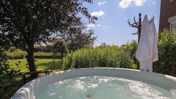 Una vasca idromassaggio con un bicchiere di champagne, immersa nel verde e decorata con una statua.