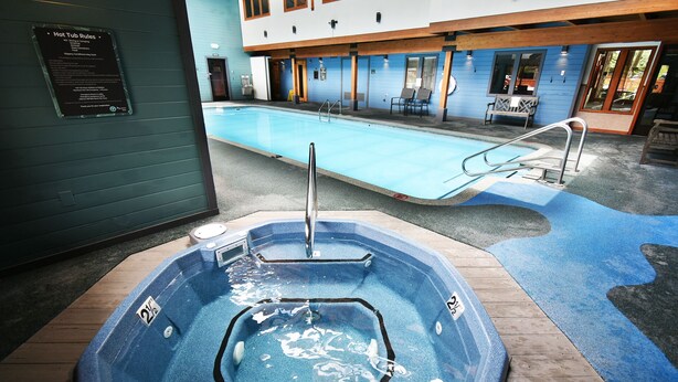 Ein Whirlpool mit Metallleiter, ein Pool mit blauer Sonnendeck und ein Gebäude mit großen Fenstern und einer blauen Außenwand.