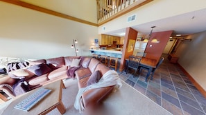 A living room with a brown leather sofa, a wooden coffee table, and a dining area with a wooden table and chairs.