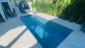 A rectangular swimming pool with a tiled deck, surrounded by greenery and outdoor seating.