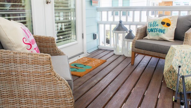 A wooden deck with wicker furniture and a cushion with a sun design.