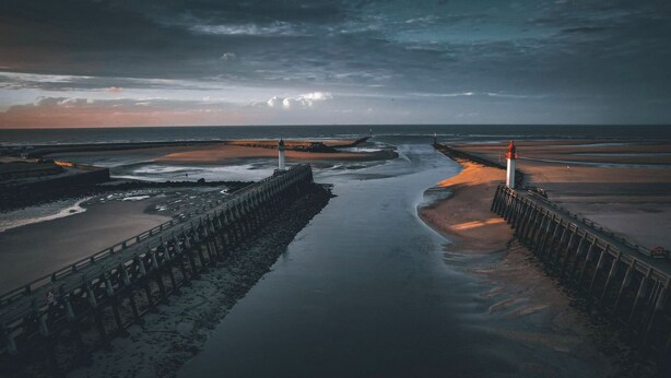 Un paysage côtier avec une jetée s’avançant dans l’eau, une plage de sable et une côte rocheuse.