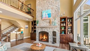 Un salón amplio con chimenea de piedra, una escalera de madera y un balcón.