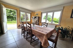 A dining area with a table, chairs, a potted plant, and a view through the open door.