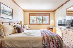 A bedroom with a large bed, a television, a dresser, and a window with curtains.