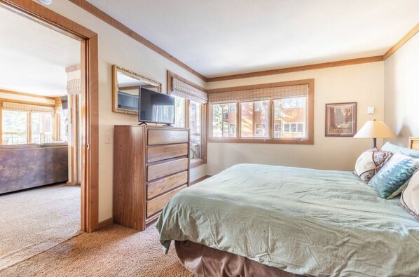 A bedroom with a bed, a dresser, a television, and a window with blinds.