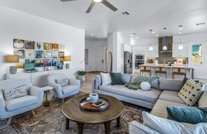 A modern living room with a sofa, armchairs, and a coffee table. There is a kitchen area with a refrigerator and a dining table.