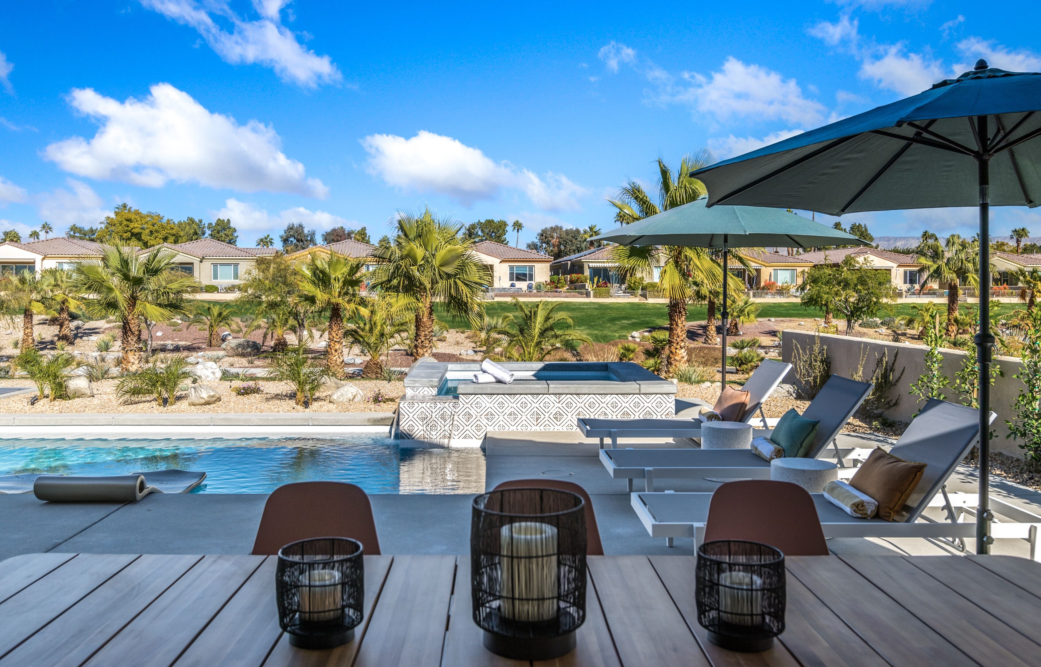 A poolside area with lounge chairs, a hot tub, and a view of a residential neighborhood.