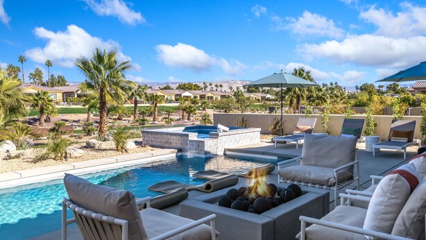 A poolside area with lounge chairs, a hot tub, and a view of a residential community.