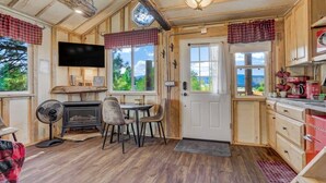 A cozy cabin interior with a fireplace, dining area, kitchen, and large windows offering a scenic view. - Heavenly Haven Treehouse (Larkspur)