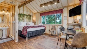 A cozy room with a bed, a dining table, chairs, a sink, and a window with a view of trees. - Heavenly Haven Treehouse (Larkspur)