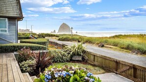 Ein Küsteneigentum mit Holzterrasse, angelegtem Garten und Blick auf Strand und Meer.