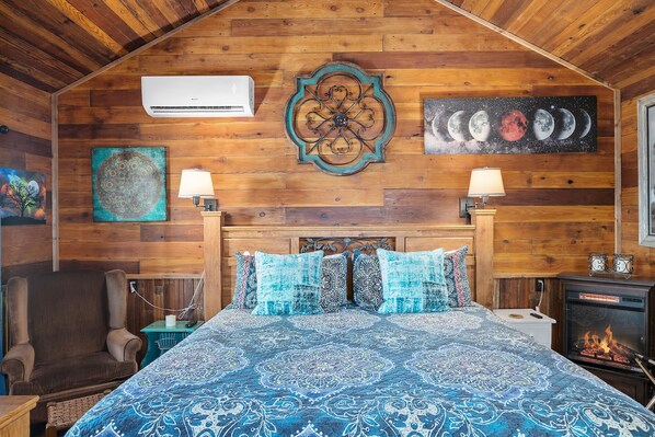 Ein gemütliches Zimmer mit Holzbalkendecke, einem Bett mit gemusterten Textilien, einer wandmontierten Klimaanlage und einem Kamin.