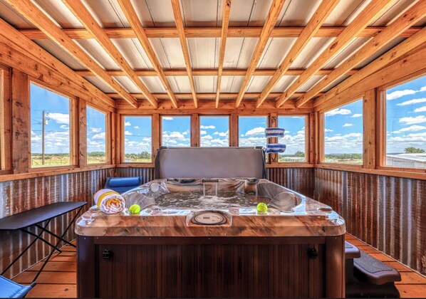 Relax in a spacious room with a large hot tub and a high ceiling, offering a view of the outdoors through large windows.